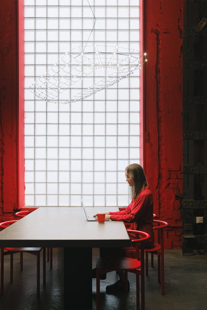 A woman works on a laptop at a red-themed, modern office desk.